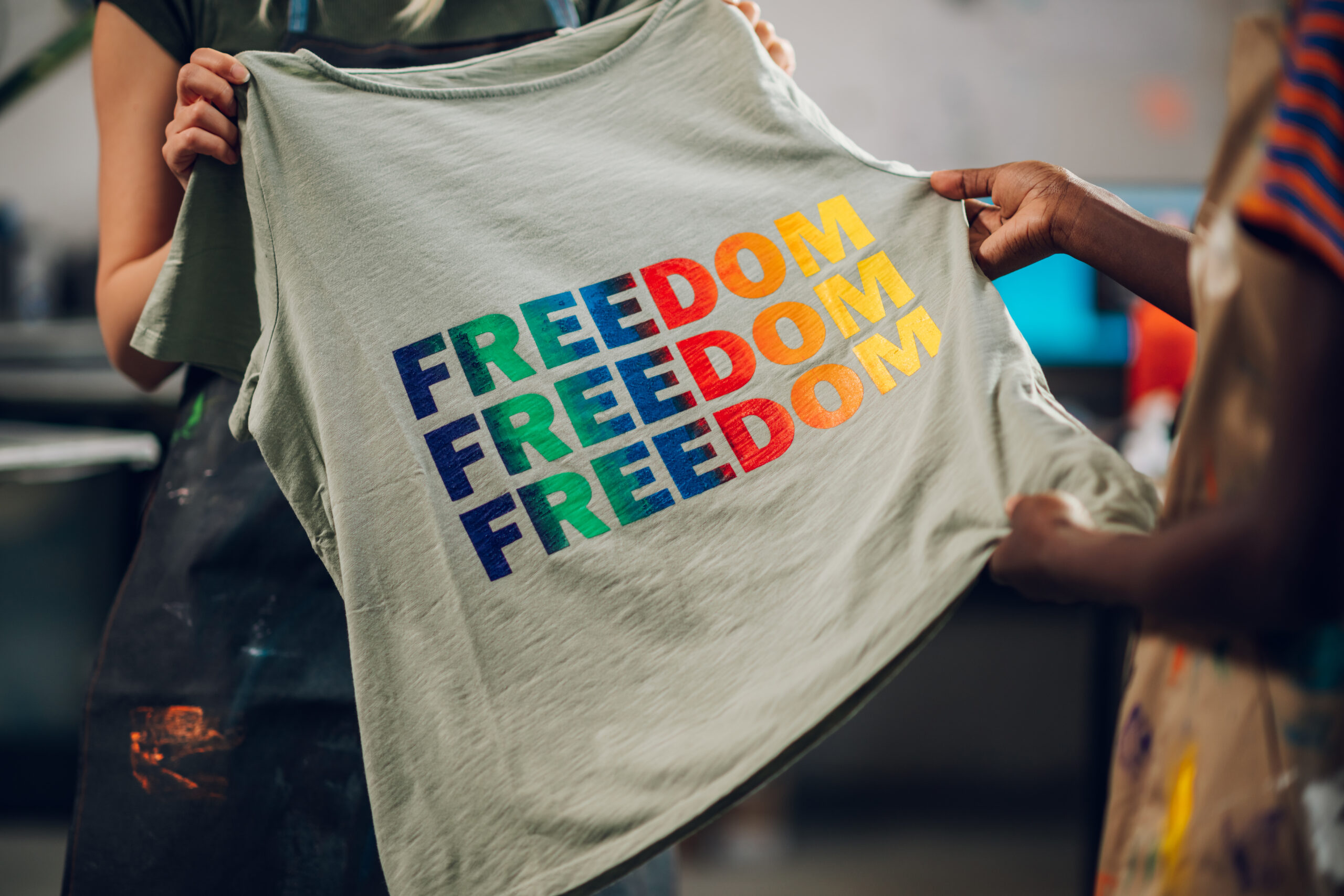 Close up of multicultural printing workshop workers' hands holding silk screen printed t-shirt and promoting lgbtq equality. Cropped picture of multiracial female workers hands holding printed shirt.