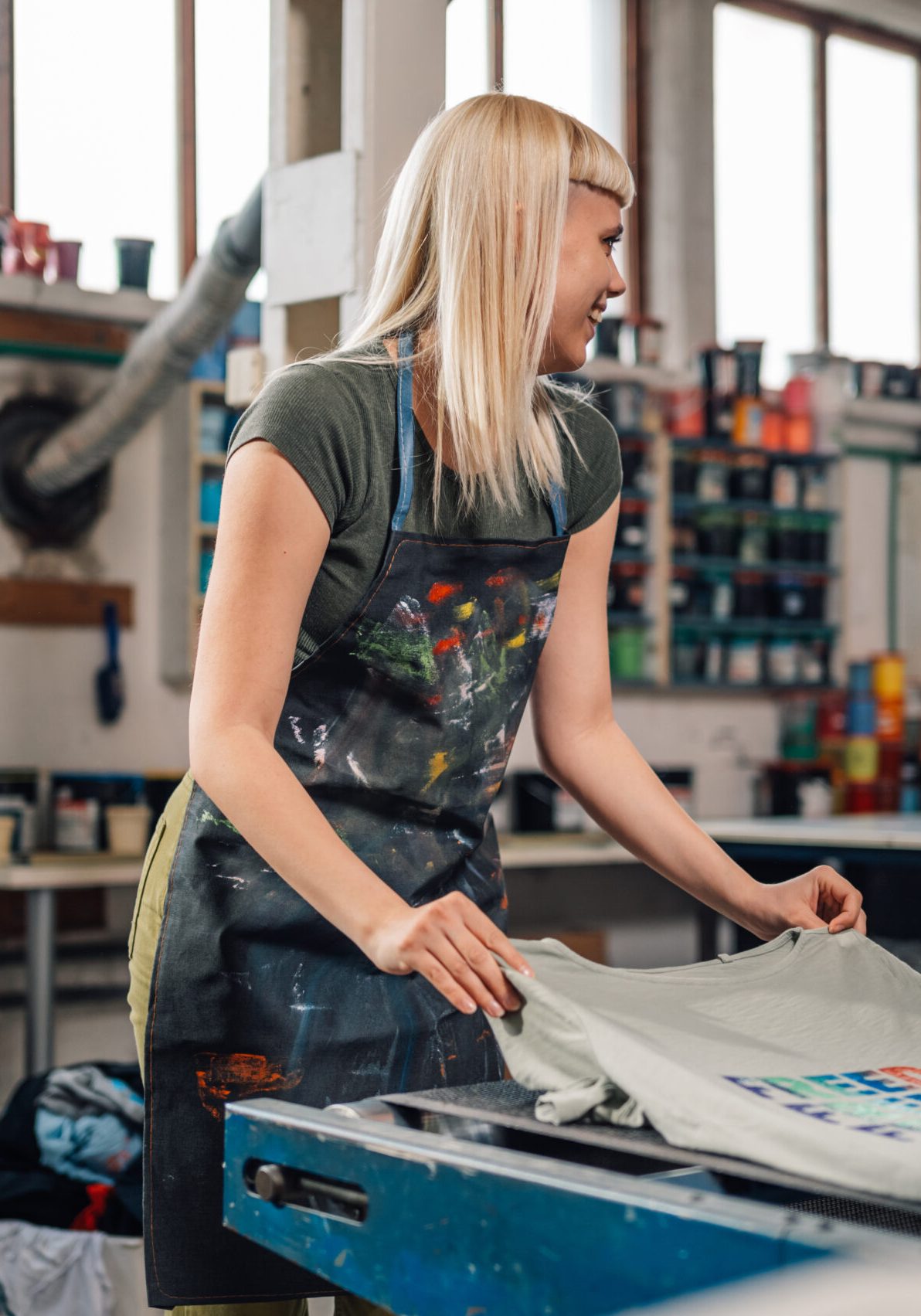 Female printer putting silkscreen printed t-shirt into drying machine.